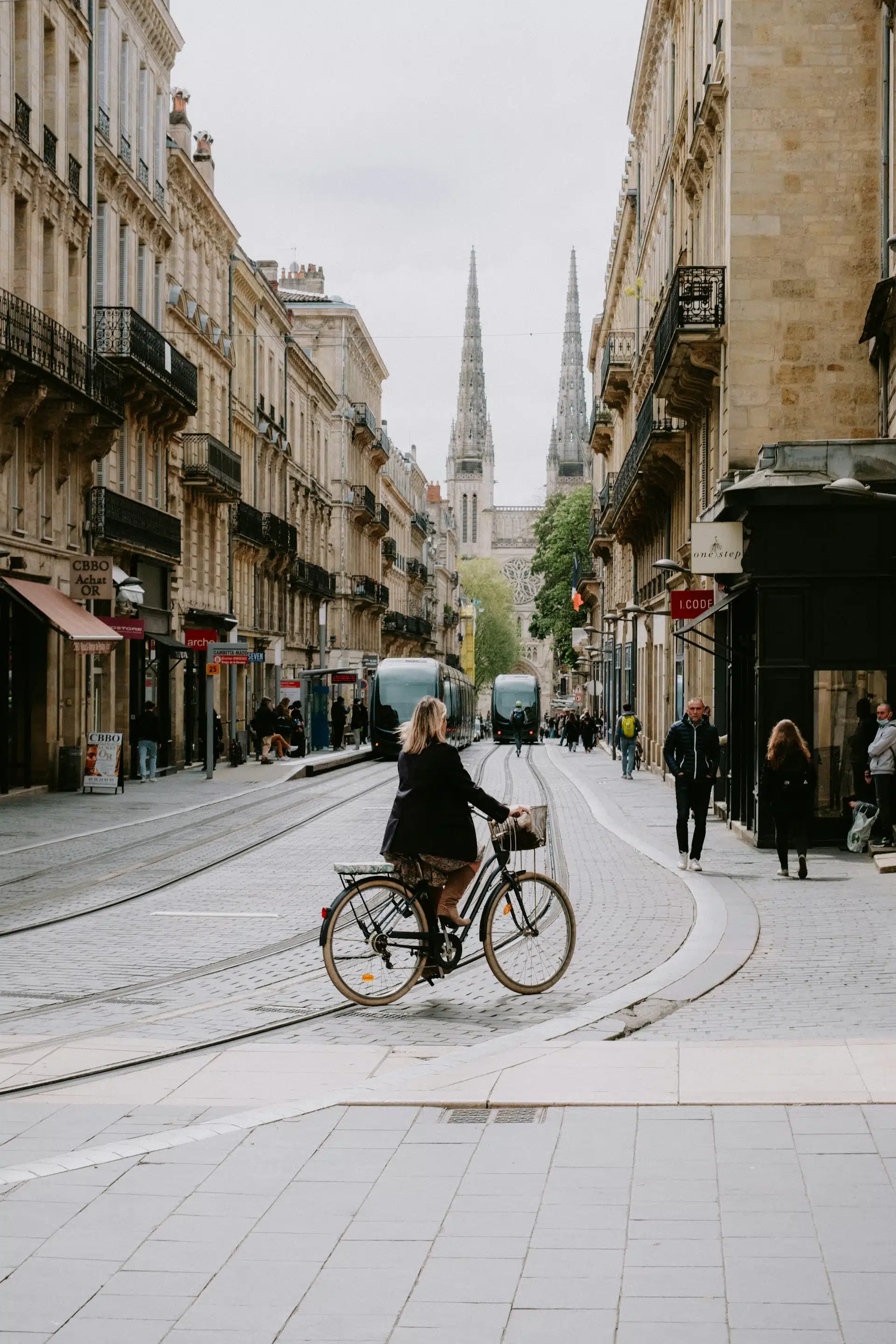 A Bordeaux street with a tram, a cyclist and the cathedral spires in the distance