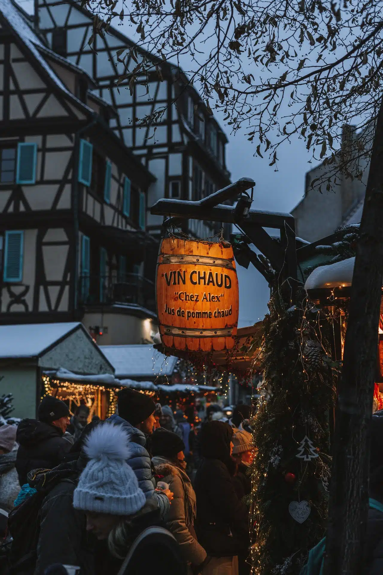 Alsace’ta yarı ahşap evlerin önünde, karla kaplı bir sıcak şarap tezgâhı: aralıkta Fransa’da bir Noel pazarı