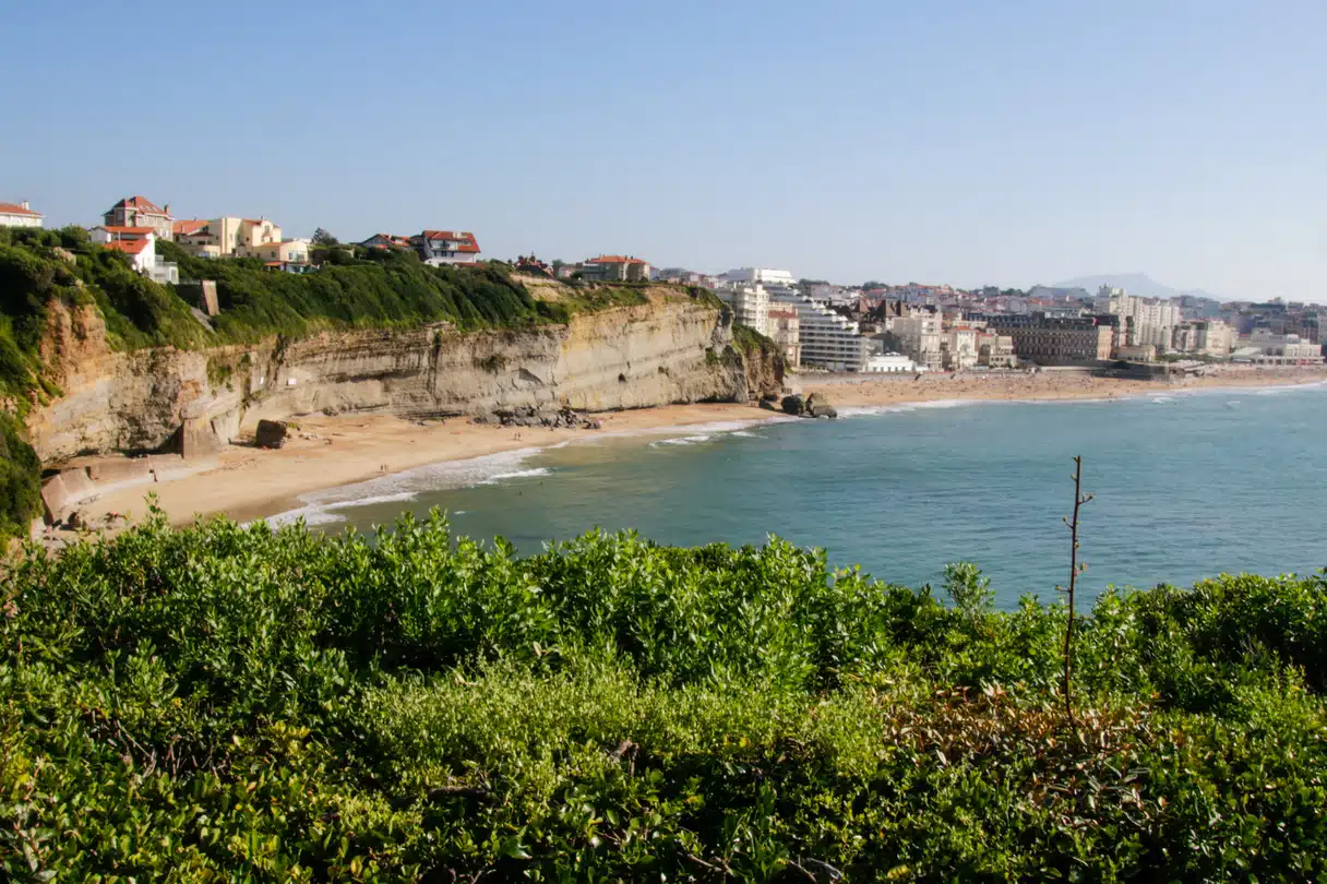Sandy cove below the cliffs at Biarritz, with the town's seafront buildings curving around the bay behind