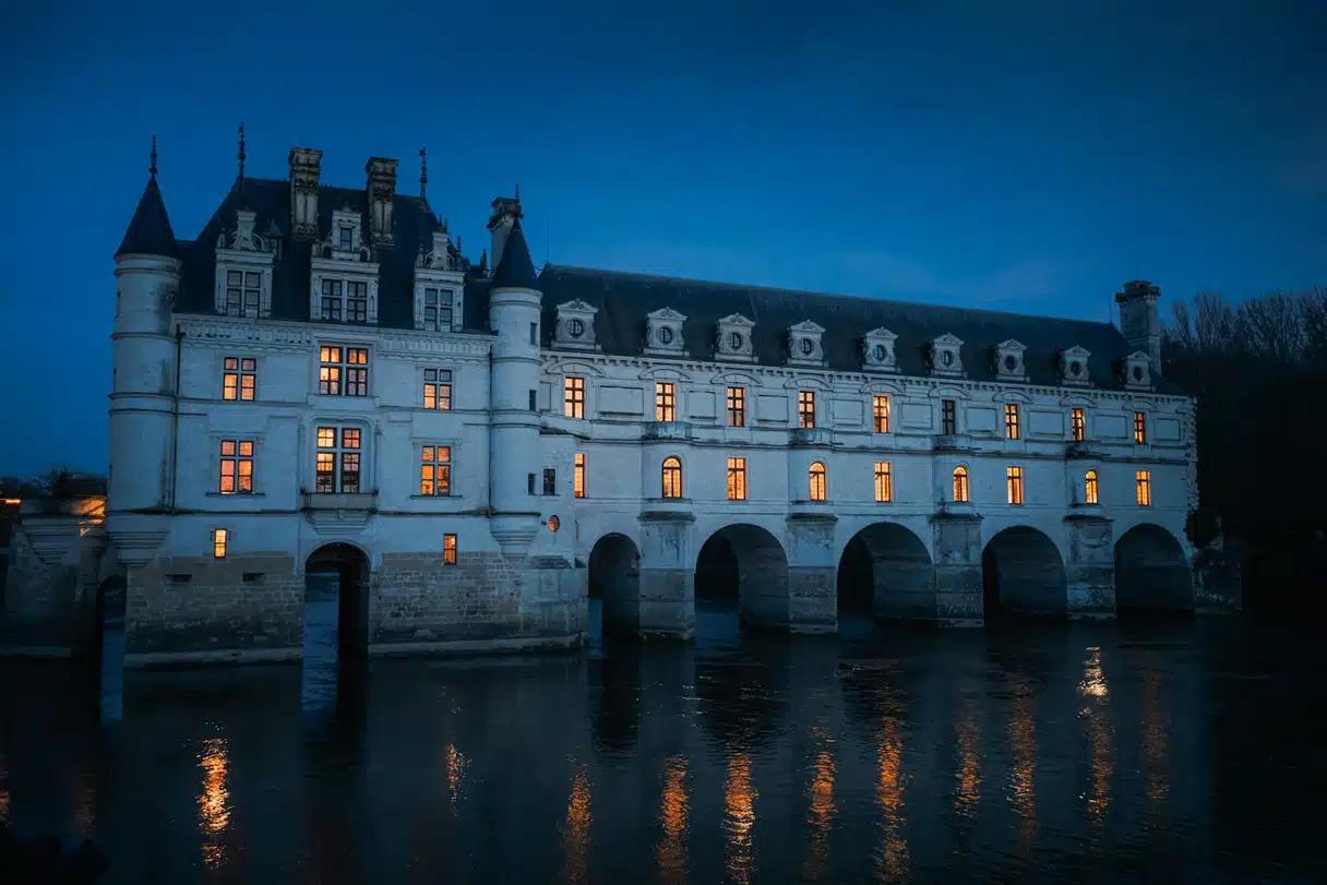 Gece çökerken Cher Nehri üzerinde uzanan Chenonceau Şatosu ve suya yansıyan ışıklı pencereleri