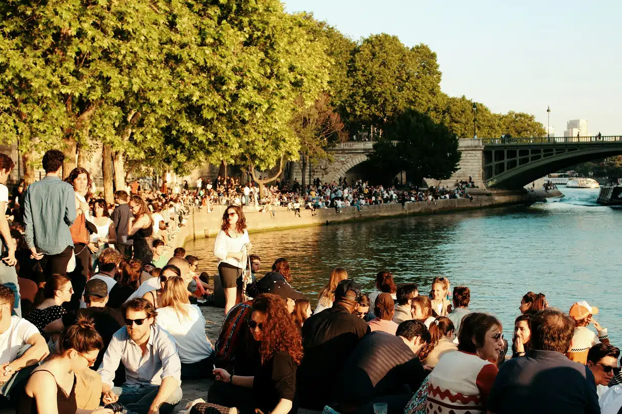 Crowds sitting shoulder to shoulder on the banks of the Seine in Paris on a sunny summer evening