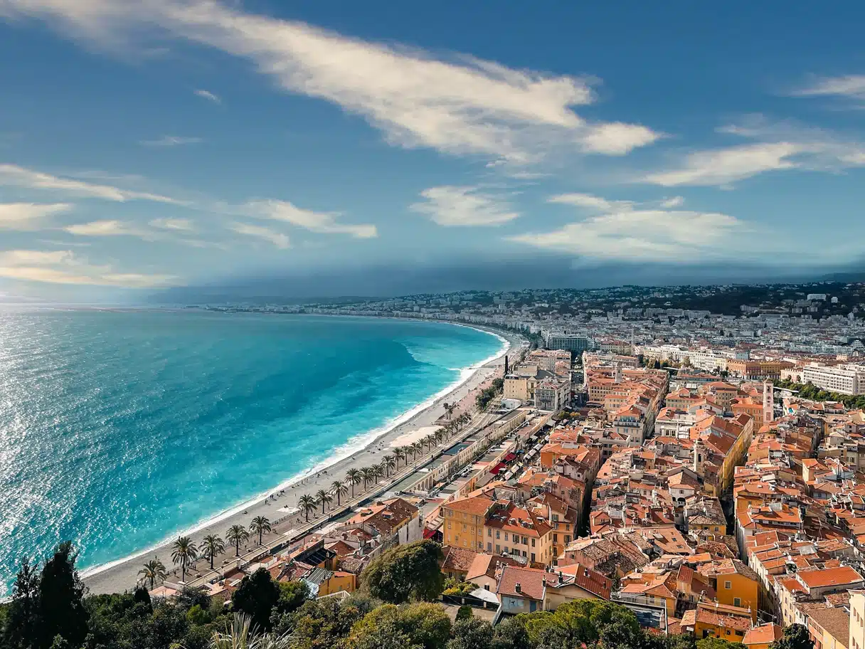 The Baie des Anges, the pebble beach and the old town rooftops of Nice seen from above, with palm trees along the Promenade des Anglais