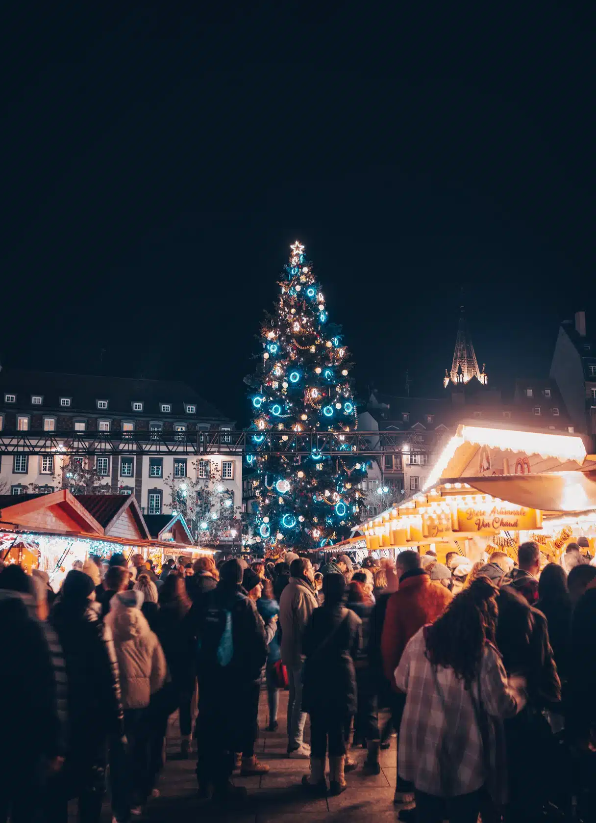 Crowds beneath the illuminated great Christmas tree at a Strasbourg Christmas market at night
