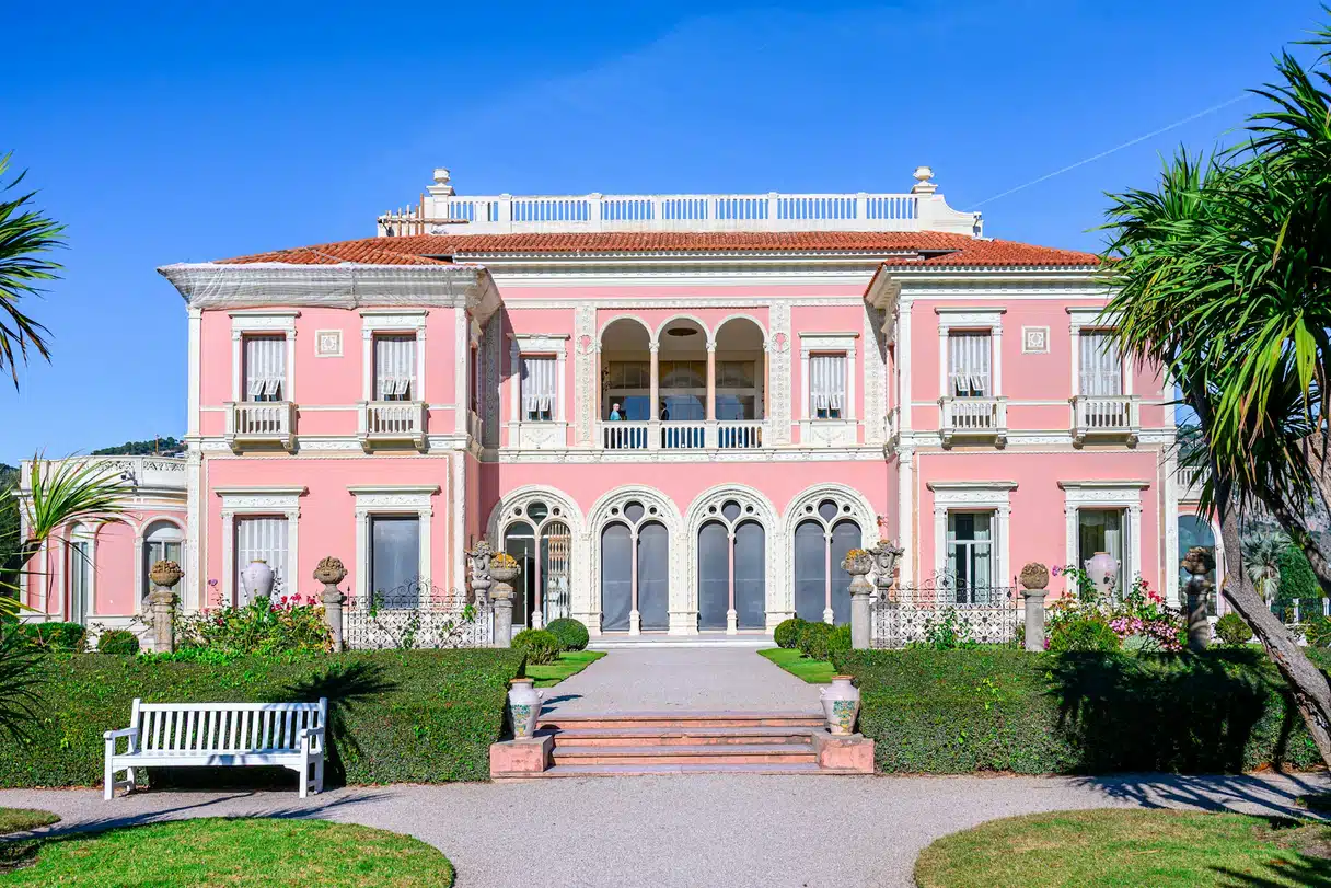 The pink facade of the Villa Ephrussi de Rothschild behind clipped hedges and lawns, at Saint-Jean-Cap-Ferrat